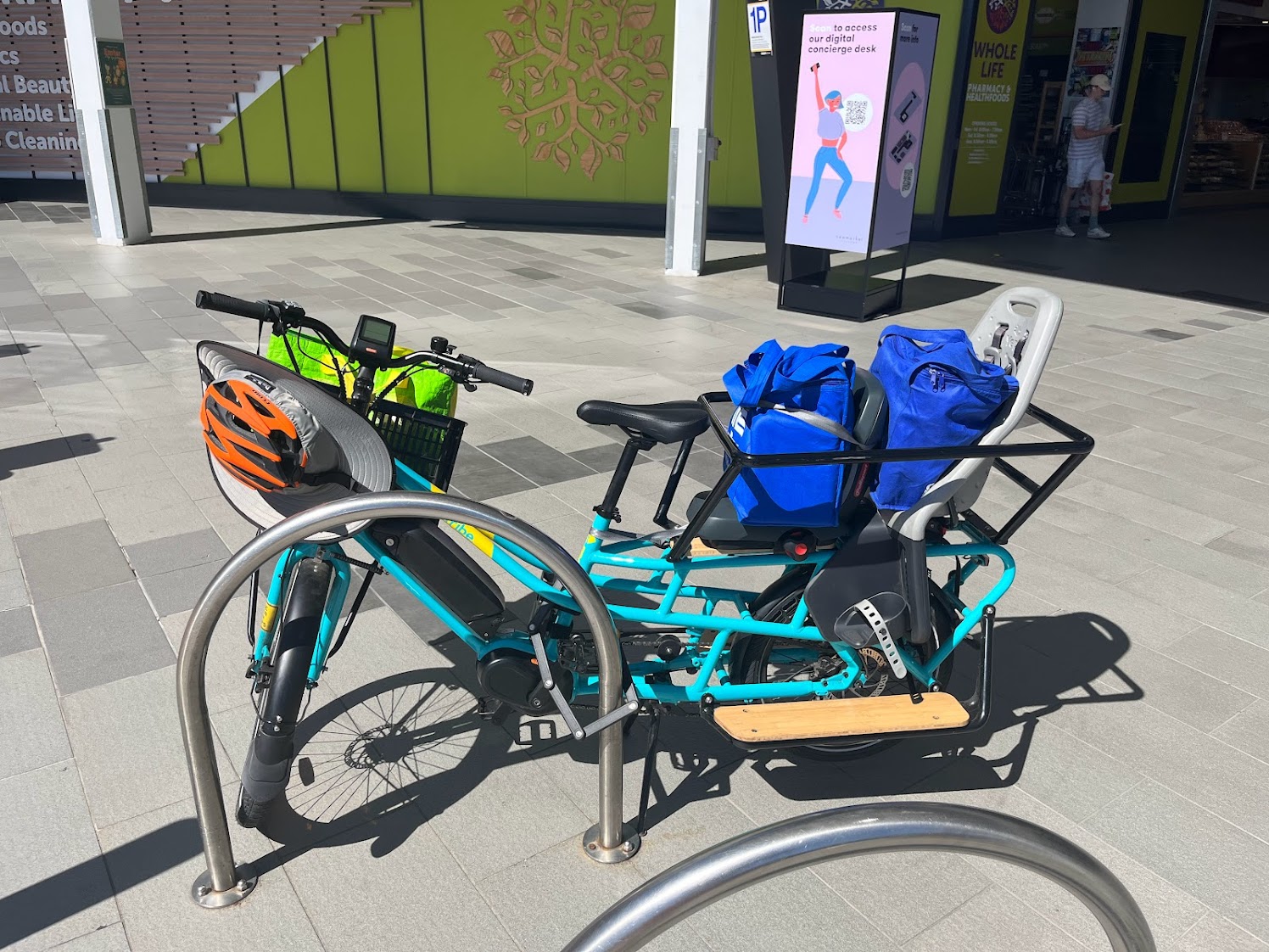 The Evamos, parked, carrying 4 large re-usable insulated shopping bags. They are distributed: two in the basket, and one in each child seat.