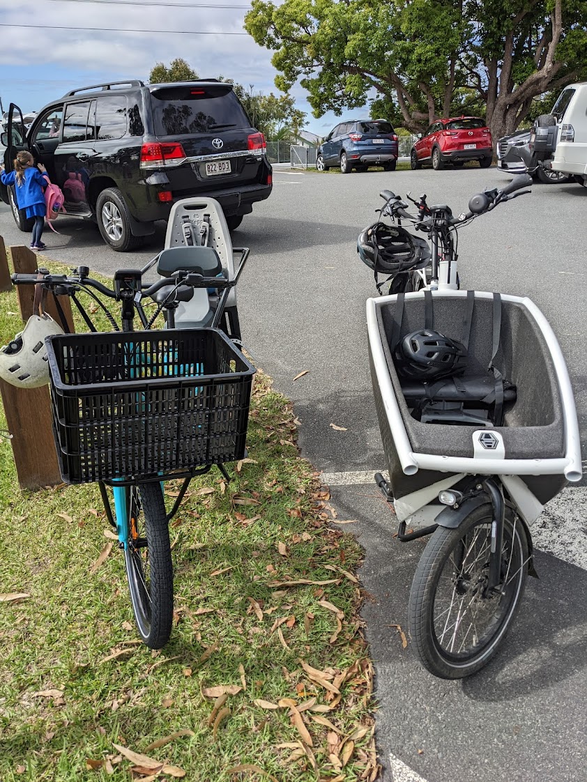 The Tribe Evamos pictured side by side with an Urban Arrow bafiets. In a school car park, front view.